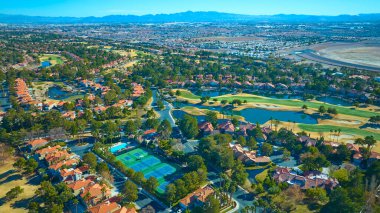 Las Vegas 'ta yemyeşil bir golf sahası, terasotta çatılı evler ve spor tesislerinin yer aldığı banliyö vahasının havadan görünüşü, hepsi de parlak güneş ışığı altında manzaralı dağların arka planına karşı kurulmuş..