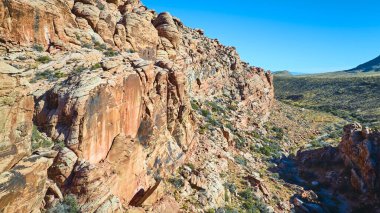 Calico, Las Vegas yakınlarındaki engebeli Red Rock uçurumlarının havadan görüntüsü. Açık mavi gökyüzü altında katmanlı tortulu kaya ve seyrek bitki örtüsü Nevada doğal güzelliği ve macerasının özünü yakalar..