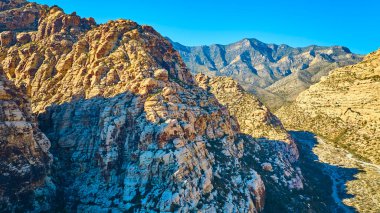 Nevada, Red Rock 'taki Ice Box Canyon' ın görkemli hava manzarası. Güneş ışığı yükselen dağların engebeli güzelliğini arttırır, bu nefes kesici çöl manzarasında macera ve keşif çağrıştırır..