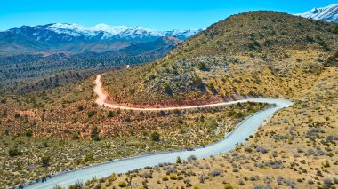 Las Vegas yakınlarındaki Charleston Dağı 'nın görkemli arka planına bakan dolambaçlı toprak bir yolun üzerindeki hava manzaralı Nevada çölünün engebeli güzelliğini keşfedin..