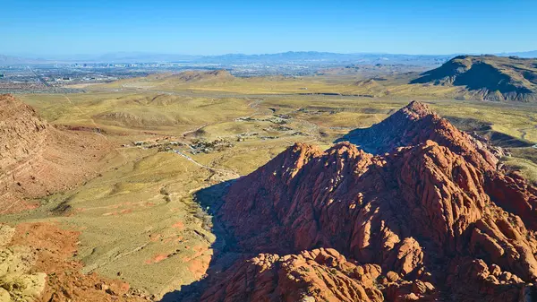 Kızıl Kaya Kanyonu 'nun göz kamaştırıcı hava manzarası, önplanda canlı oluşumlar ve uzaktan Las Vegas silueti. Nevada ikonik manzarasında çöl güzelliği ve kentsel karşıtlığı tecrübe edin.