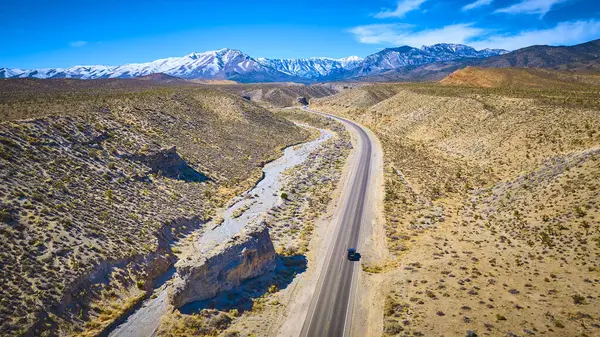 Las Vegas yakınlarındaki dolambaçlı bir çöl yolunda, Nevada, Charleston Dağı 'nın karlı zirvelerine doğru giden yalnız bir aracın hava görüntüsü, engebeli güzellikler arasında sakin bir yolculuk sergiliyor..