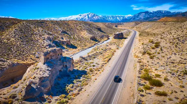 Las Vegas yakınlarındaki bir çöl yolunda tek başına bir araç engebeli araziyi parlak mavi bir gökyüzünün altından geçiyor. Karla kaplı Charleston Dağı heybetli duruyor, muhteşem bir macera arkaplanı sunuyor ve