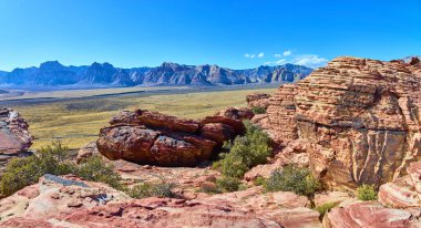 Las Vegas yakınlarındaki Red Rock Kanyonu 'nun nefes kesici manzarası. Güneşli kırmızı kumtaşı oluşumları ve sivri dağlara karşı seyrek yeşillik doğal güzellik ve macera manzarası yaratır..