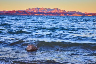 Nevada Mead Gölü 'nde altın saat yumuşak dalgalarla çevrili sakin bir deniz manzarası yakalar. Güneş görkemli dağların ardında batar, göğü sıcak renklerle boyar, huzur verir.