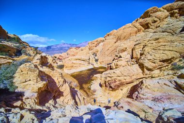 Yürüyüşçüler Las Vegas, Nevada yakınlarındaki Red Rock Kanyonu 'ndan geçiyor. Canlı kumtaşı oluşumları ve berrak mavi gökyüzü doğada macera ve keşif için çarpıcı bir zemin oluşturur..