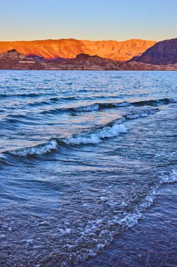 Gün batımında Mead Gölü 'nün dingin güzelliğinin tadını çıkarın. Dalgalar, altından bir gökyüzünün altındaki engebeli Nevada dağlarına doğru dalgalanır. Huzur uyandırmak ve seyahat veya sağlık temalarında kaçmak için mükemmel..