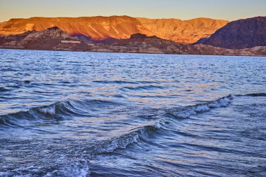 Boulder City Nevada 'daki Mead Gölü' nün üzerinde altın saat parlıyor. Yumuşak dalgalar ve engebeli dağlar doğal rahatlama ve macera temaları için mükemmel bir sahne oluşturur..