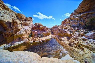 Las Vegas, Nevada 'daki çarpıcı Calico Tanklarını keşfedin. Parlak mavi bir gökyüzünün altında sakin bir göleti çevreleyen engebeli kırmızı kaya oluşumlarına hayret. Seyahat ve macera meraklıları için mükemmel..