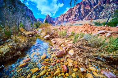 Las Vegas, Nevada 'daki Pine Creek Kanyonu' nun dingin güzelliğini keşfedin. Açık bir akıntı canlı gökyüzünü yansıtırken görkemli kızıl kaya oluşumları bu sakin çöl kontrastında çarpıcı bir kontrastlık yaratır.