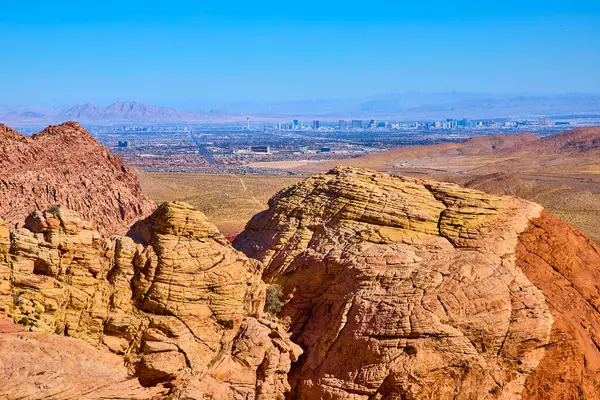Calico Tank Yolu 'ndan göz kamaştırıcı manzara: Kırmızı Kaya Kanyonu' nun canlı kırmızı ve sarı kumtaşı oluşumları parlak mavi gökyüzünün altında Las Vegas silueti ile buluşuyor. Doğa ve şehir mükemmel bir uyum içinde..