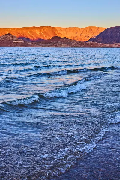 Gün batımında Mead Gölü 'nün dingin güzelliğinin tadını çıkarın. Dalgalar, altından bir gökyüzünün altındaki engebeli Nevada dağlarına doğru dalgalanır. Huzur uyandırmak ve seyahat veya sağlık temalarında kaçmak için mükemmel..