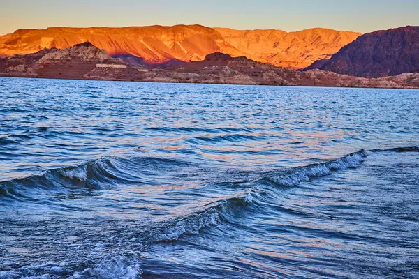 Boulder City Nevada 'daki Mead Gölü' nün üzerinde altın saat parlıyor. Yumuşak dalgalar ve engebeli dağlar doğal rahatlama ve macera temaları için mükemmel bir sahne oluşturur..