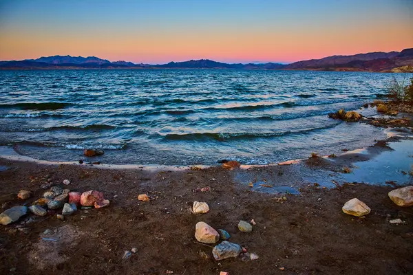 Gün batımında Meads Gölü 'nün kayalık kıyı şeridinin huzurlu güzelliğini hissedin. Altın saat, gökyüzünü turuncu ve pembe renklerle boyuyor Nevada dağlarının uzak siluetlerini çerçeveliyor..
