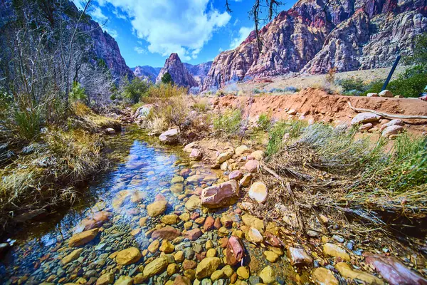 Las Vegas, Nevada 'daki Pine Creek Kanyonu' nun dingin güzelliğini keşfedin. Açık bir akıntı canlı gökyüzünü yansıtırken görkemli kızıl kaya oluşumları bu sakin çöl kontrastında çarpıcı bir kontrastlık yaratır.