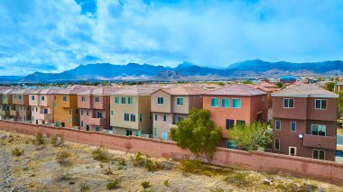 Las Vegas, Nevada 'daki modern banliyö evlerinin havadan görünüşü, tuğladan bir duvarla engebeli bir çöl manzarasının arasına kurulmuş. Arka planda görkemli dağlar ve parçalı bulutlu gökyüzü var..