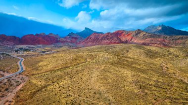 Nevadas Red Rock Kanyonu 'nun havadan görünüşü: dolambaçlı bir yol açık mavi gökyüzü altında canlı kırmızı oluşumlara öncülük eder. Yolculuk macerasının özünü yakalamak için mükemmel..