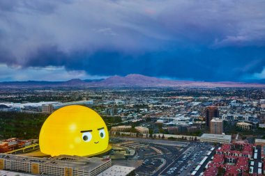 Las Vegas 'ın havadan görünüşü. Uzakta büyük kumarbazın olduğu, emojiden esinlenilmiş dev bir bina. Dramatik gökyüzü, canlı şehir manzarası üzerinde yaklaşan fırtınaya işaret ediyor..