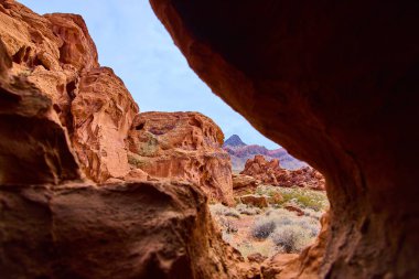 Nevada, Boulder City yakınlarındaki çarpıcı Redstone Dune 'u keşfedin. Açık mavi gökyüzüne karşı bir mağara tarafından çerçevelenmiş canlı kırmızı kaya oluşumlarına hayret etmek macerayı ve doğanın güzelliğini çağrıştırıyor..