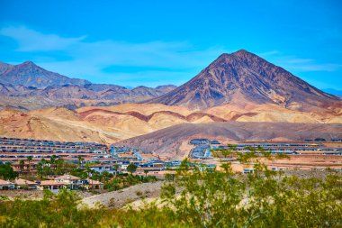 Henderson Nevada 'daki güneşli çöl manzaraları çarpıcı bir dağ zeminini ve banliyö evlerini gözler önüne seriyor. Bu sakin sınır manzarasında engebeli doğa ile modern yaşam arasındaki zıtlığı vurguluyor.