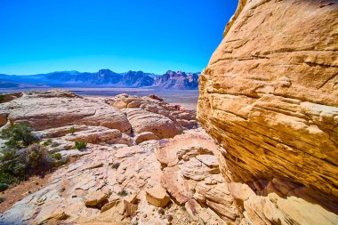 Las Vegas, Nevada 'daki Red Rock Kanyonu' nun görkemli güzelliğini yakalayın. Güneşli kaya oluşumları ve uzak dağlar canlı mavi gökyüzüne karşı çöl manzarasının zamansız cazibesini resmediyor..