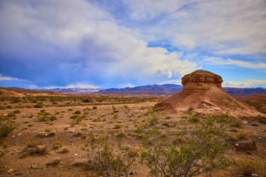 Boulder City çölünün kurak alanından yükselen büyük bir kayanın nefes kesici manzarası. Dramatik gökyüzü ve dayanıklı bitki örtüsü Nevadas 'ın doğal manzarasının ebedi güzelliğini vurgular..