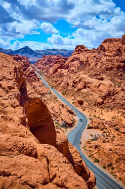 Nevadas Ateş Vadisi 'nin engebeli güzelliğini keşfedin. Kızıl kaya oluşumları parlak mavi gökyüzünün altında dolambaçlı bir yol oluşturur. Bu nefes kesici çöl manzarasında yalnızlığı ve macerayı tecrübe edin..