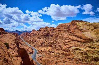 Nevadas Ateş Vadisi 'ndeki büyüleyici Moapa Vadisi' ni keşfedin. Kıpkırmızı kaya oluşumlarından geçen dolambaçlı bir yol, parlak mavi gökyüzü altında tüylü bulutlarla maceraya ve yalnızlığa davetiye çıkarır..