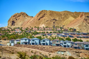 Engebeli çöl tepeleri ve canlı mavi gökyüzü çerçeveli Henderson, Nevada 'daki modern banliyö evleri, doğal güzellikler arasında yaşayan kentsel yaşamın zıtlığını ve uyumunu vurguluyor..