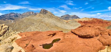 Kızıl Kaya Kanyonu, Nevada 'nın havadan görünüşü: Pas rengi kumtaşı oluşumları ve nadir bir su havuzu açık mavi gökyüzü altında dramatik bir manzara yaratır. Doğa, jeoloji ve seyahat için mükemmel..