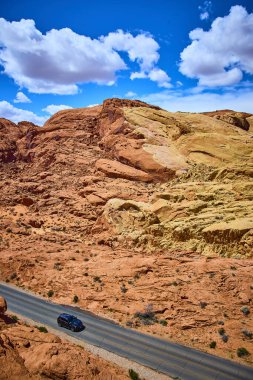 Nevada Moapa Vadisi 'ndeki Ateş Vadisi' nin çarpıcı kırmızı kaya oluşumlarını tek başına geçen bir araba. Canlı mavi gökyüzü ve geniş çöl manzarası macera ve keşiflere ilham verir. Tam oldu.