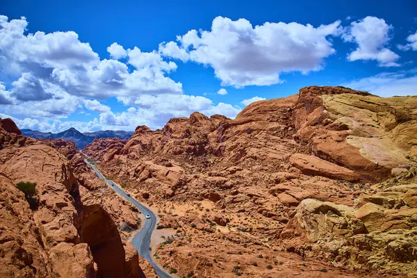Nevadas Ateş Vadisi 'ndeki büyüleyici Moapa Vadisi' ni keşfedin. Kıpkırmızı kaya oluşumlarından geçen dolambaçlı bir yol, parlak mavi gökyüzü altında tüylü bulutlarla maceraya ve yalnızlığa davetiye çıkarır..