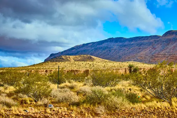 Görkemli Red Rock Kanyonu Las Vegas Nevada 'da dramatik bir gökyüzünün altında sergileniyor. Yuvarlanan tepelerden ve seyrek bitkilerden oluşan engebeli bir çöl manzarası macera ve doğal güzelliğin ruhunu yakalar..