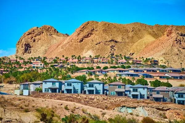 Engebeli çöl tepeleri ve canlı mavi gökyüzü çerçeveli Henderson, Nevada 'daki modern banliyö evleri, doğal güzellikler arasında yaşayan kentsel yaşamın zıtlığını ve uyumunu vurguluyor..