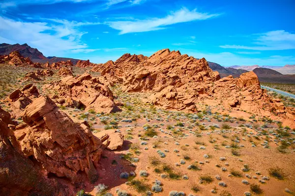 Nevada, Redstone Dune 'un nefes kesici kırmızı kumtaşı oluşumlarını keşfedin. Bir yol, parlak mavi gökyüzünün altındaki engin çöl manzaralarında maceraya davetiye çıkarır. Seyahat ve doğa temaları için mükemmel..