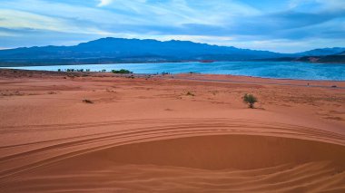 Utah Kasırgası yakınlarındaki Sand Hollow Gölü 'nün mavi sularıyla gündoğumunda uzak dağların birleştiği canlı kum tepelerinin hava görüntüsü. Seyahat macerası ve doğal güzellik temaları için mükemmel..