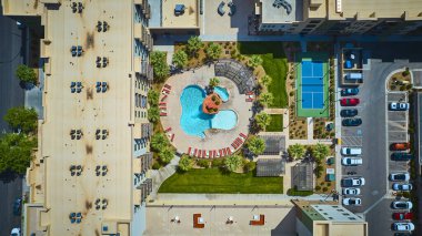 Bir tatil köyü tarzı yüzme havuzu, bereketli palmiye peyzajı ve lüks şehir yaşamı için parlak öğle güneşi altında canlı bir mavi tenis kortu içeren modern bir St George Utah apartmanı manzarası.