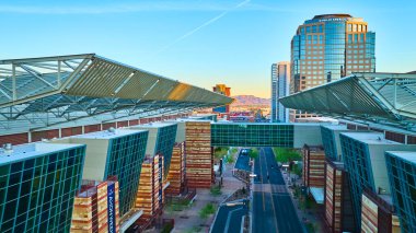 Phoenix Arizona şehir merkezinin altın saatindeki hava manzarasında çarpıcı kongre merkezi modern şehir altyapısı ve arkasında dağlar ve açık gökyüzü bulunan Bank of America kulesi yer alıyor.