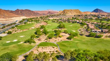 Las Vegas Gölü 'ndeki lüks golf sahasının ve lüks evlerin havadan görünüşü ve açık mavi gökyüzü altında çöl manzarasıyla ve manzaralı dağlarla çelişen yeşil çimenli yollar.