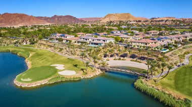 Las Vegas Gölü 'nde yemyeşil bir golf sahası ve ışıl ışıl bir göl çevreleyen lüks evleri ve arka planda çöl dağlarını gösteren lüks tatil beldesi manzarası ve manzaralı güzellik.