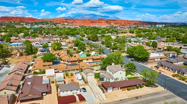 St. George Utah 'ın canlı bir banliyö mahallesinin havadan görünüşü. Renkli evler, ağaçlarla kaplı sokaklar ve parlak mavi gökyüzünün altında çarpıcı kızıl kaya birikimleri.