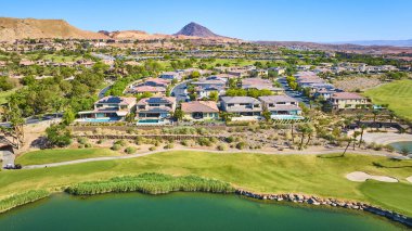 Las Vegas Gölü 'nde yemyeşil bir golf sahası ve sakin bir gölün sınırındaki lüks evlerin havadan görünüşü. Arka planda lüks emlak ve seyahat için ideal çöl dağları var.