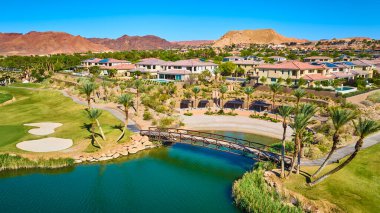 Las Vegas Nevada Gölü 'nde yemyeşil bir golf sahası ve göl kenarındaki terakotta çatısı olan lüks evlerin havadan görünüşü çarpıcı çöl dağları çarpıcı bir tatil köyü tarzı yaratıyor.