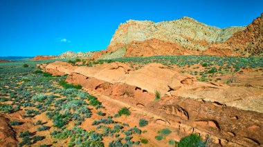 Utah Kasırgası yakınlarındaki Babil Kemeri 'nin hava manzarasında canlı kırmızı kaya oluşumları engebeli dağlar ve engebeli çöl bitkileri açık mavi gökyüzü altında açık hava macerası ve doğa temaları için idealdir.