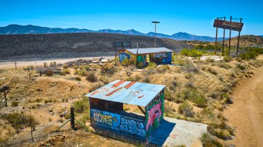 Terk edilmiş duvar yazısıyla kaplı binalar ve Arizona çölünde ıssız bir tabela, açık mavi gökyüzünün altında çalılıklar ve dağlarla çevrili, kentsel çürümeyi çağrıştıran ve unutulmuş