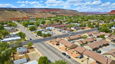 Güneşli bir günde açık mavi gökyüzünün altında, arka planda yeşil ağaçlar ve çarpıcı kızıl kaya oluşumlarıyla St. George Utah 'ta huzurlu bir banliyö manzarası.