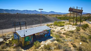 Terk edilmiş duvar yazısıyla kaplı bir bina ve solmuş yol tabelaları arka planda dağları olan kuru bir Arizona çölünde güneybatıda unutulmuş Amerika 'yı simgeliyor.