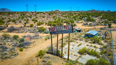 Terk edilmiş bir Arizona çöl sahnesinin havadan görünüşü yıpranmış bir reklam panosu, grafiti kaplı bir bina ve açık mavi gökyüzünün altındaki uzak elektrik hatları izolasyonu ve çürümeyi yakalıyor.