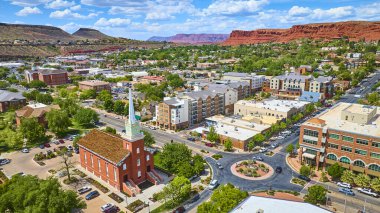 St. George Utah şehir merkezinin havadan görünüşü, tarihi kırmızı tuğla kilise ve saat kulesi, kırmızı kayaların çerçevelediği yoğun bir kavşakta parlak mavi gökyüzü manzarası ve doğal güzellik.