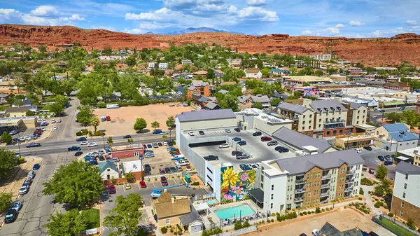 St George Utah şehir merkezinin canlı hava manzarası renkli bir duvar resmi modern apartman kompleksi ve arkasında ikonik kırmızı kaya kayalıkları olan bir havuz parlak mavi gökyüzünün altında.